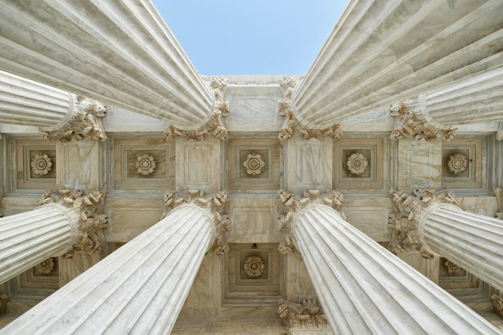 Marble columns and a coffered ceiling seen from below against a clear sky